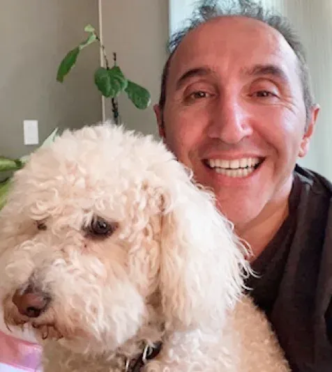 A team member smiling with his white poodle at home